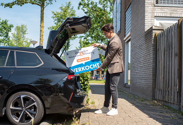 Makelaar die een verkochtbord in zijn auto stopt